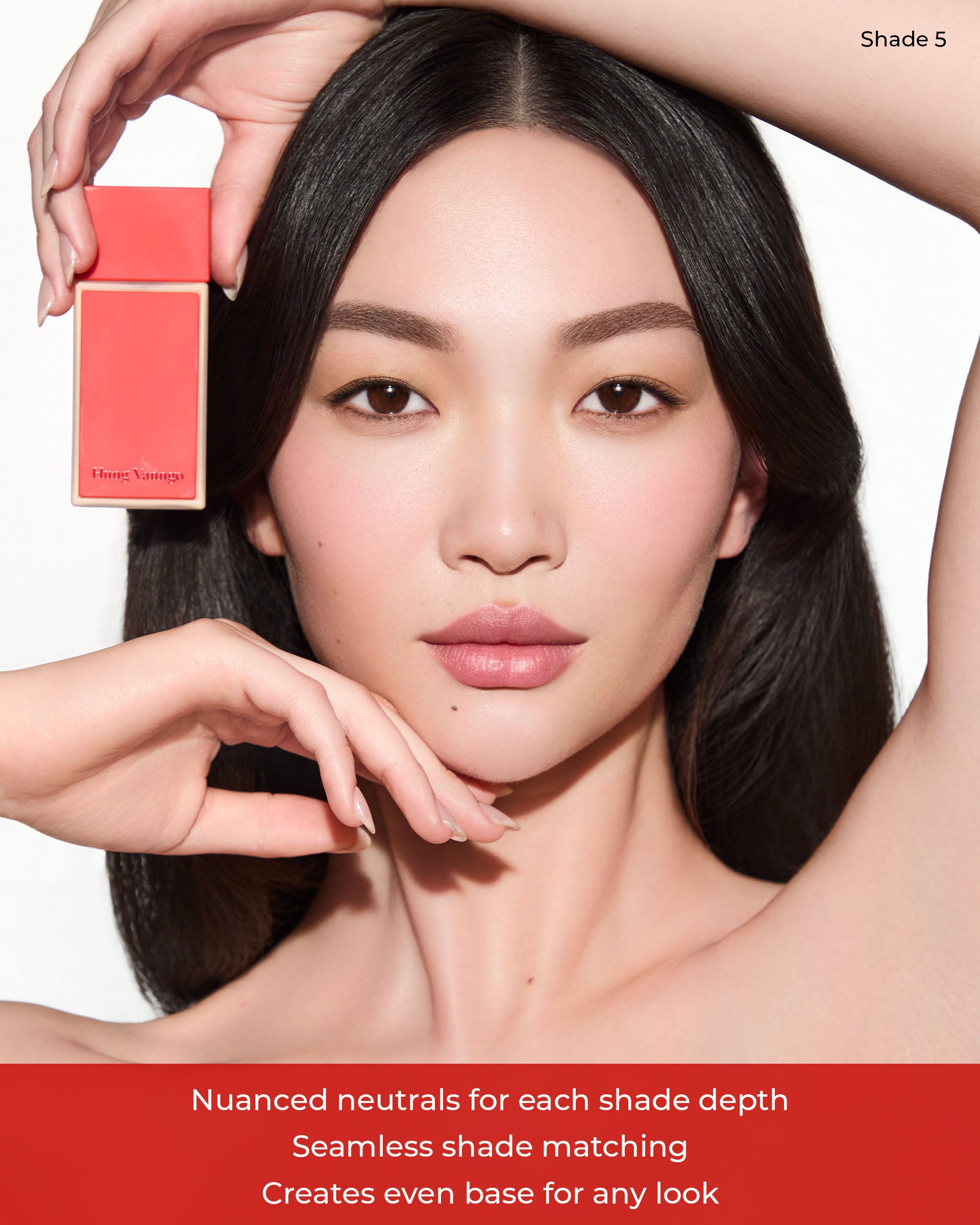 A close-up beauty shot of a woman with dark hair wearing Hung Vanngo Beauty makeup, holding a foundation package next to her face
